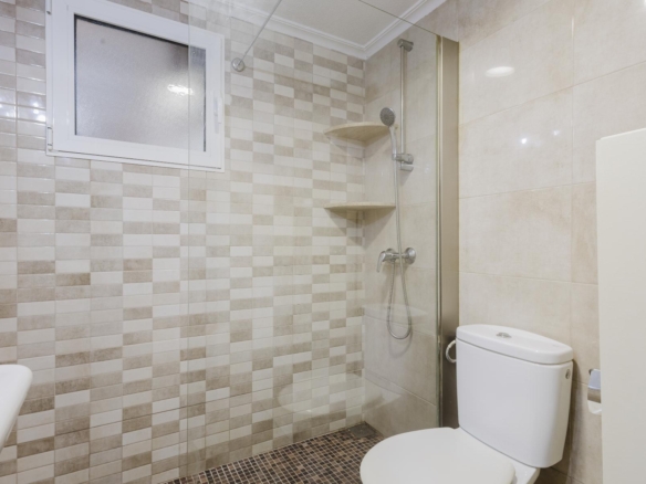 Modern bathroom with beige tiled shower area, frosted window, handheld shower, and a white toilet.