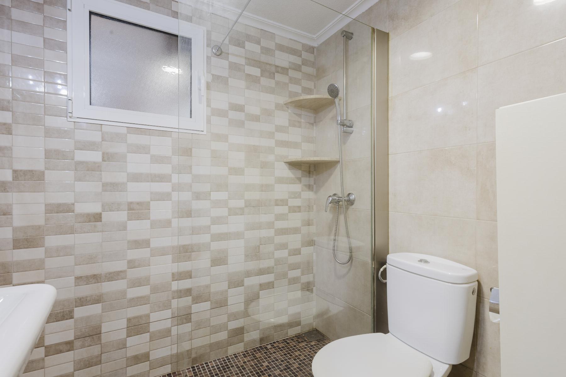 Modern bathroom with beige tiled shower area, frosted window, handheld shower, and a white toilet.