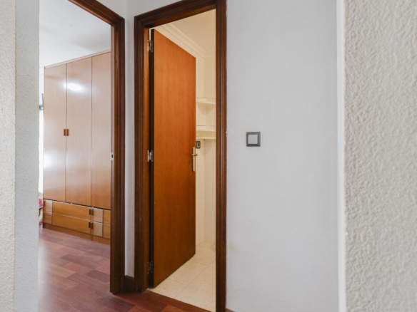 Open doorway in a hallway with dark wood trim; a tall wooden wardrobe is visible in the next room and a white shelf/closet area is beyond the door.