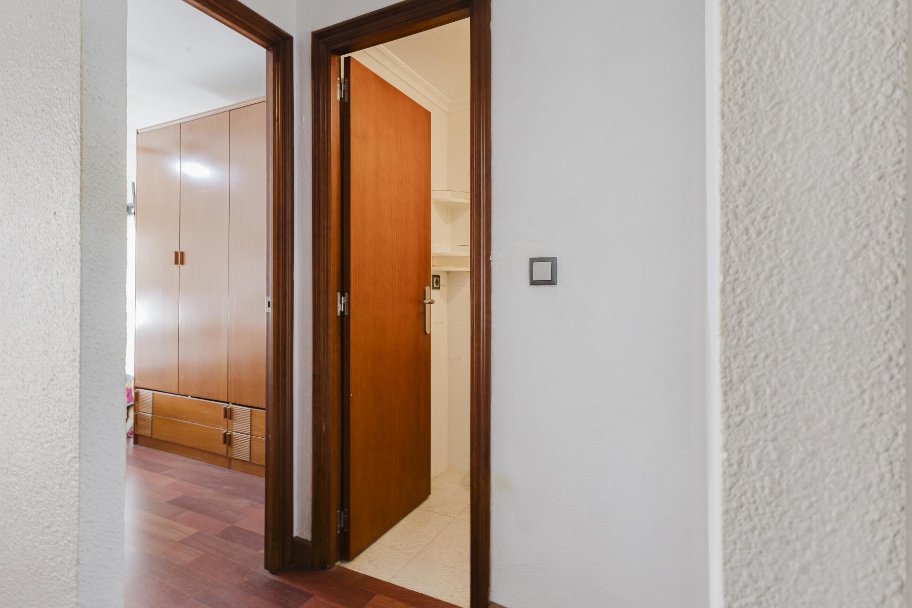 Open doorway in a hallway with dark wood trim; a tall wooden wardrobe is visible in the next room and a white shelf/closet area is beyond the door.