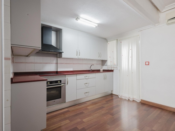 Modern L-shaped kitchen with white cabinets, red countertops, and a stainless steel oven with range hood above it.