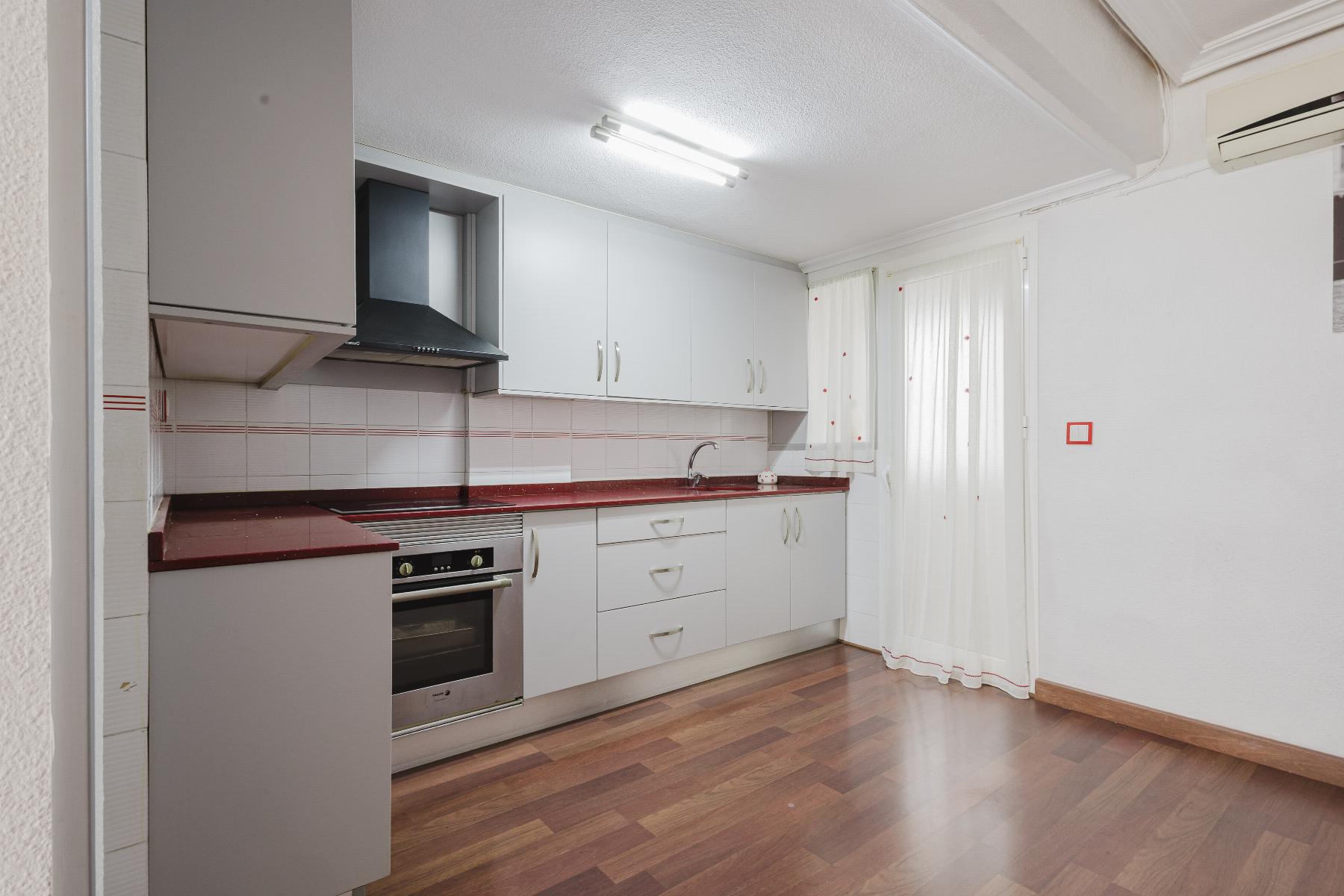 Modern L-shaped kitchen with white cabinets, red countertops, and a stainless steel oven with range hood above it.