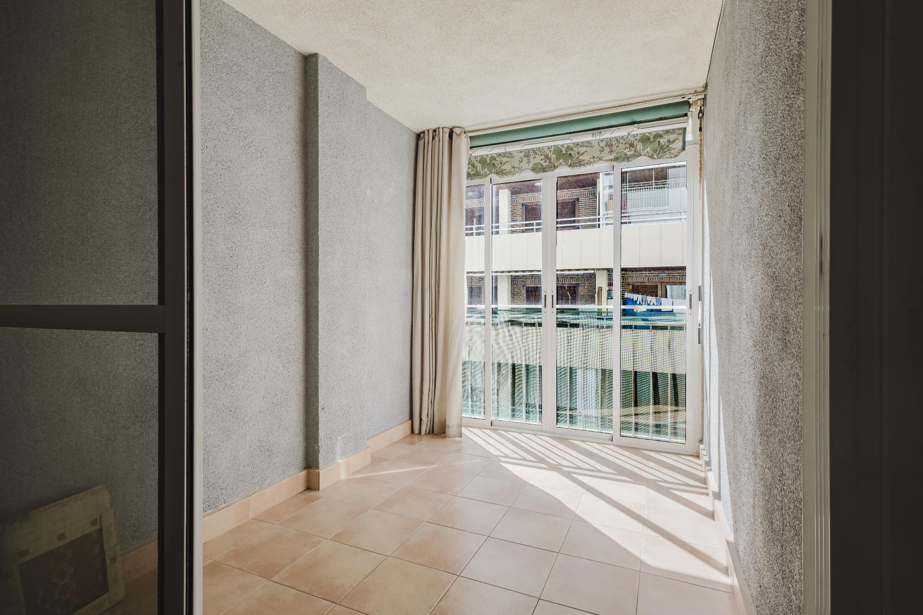 Sunlit balcony with beige tiled floor, gray walls, and large sliding glass doors opening to an outdoor pool area.