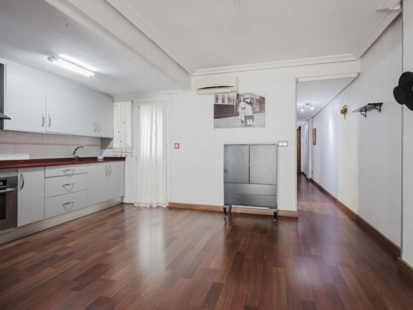 Open-plan kitchen with white cabinets and a red countertop, stainless oven, and wooden floors; hallway to the right.