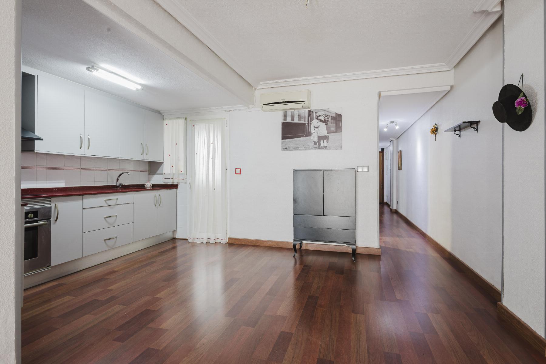 Open-plan kitchen with white cabinets and a red countertop, stainless oven, and wooden floors; hallway to the right.