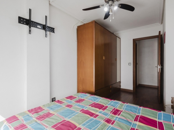 Bedroom with colorful plaid bedspread, wooden wardrobe, and an open door leading to a hallway; ceiling fan overhead