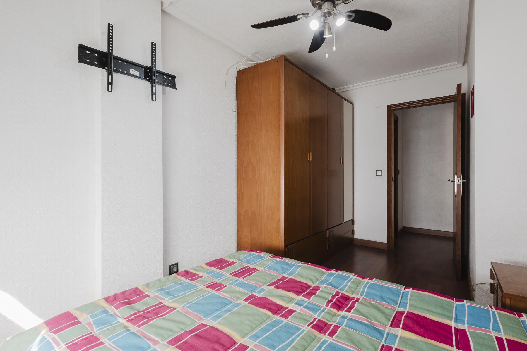Bedroom with colorful plaid bedspread, wooden wardrobe, and an open door leading to a hallway; ceiling fan overhead