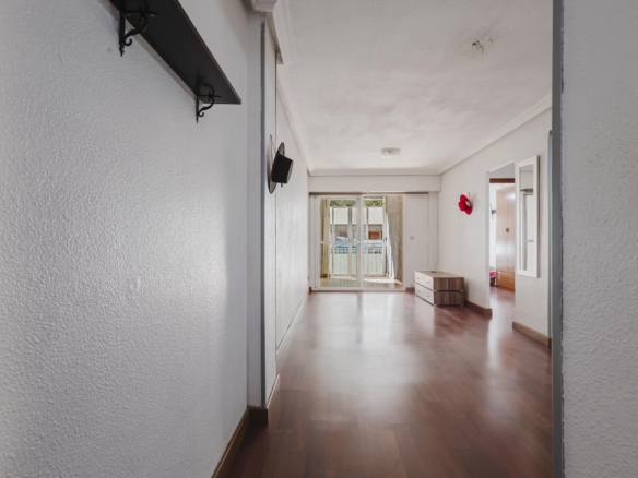 Bright hallway with wood floor leading to glass doors opening to a balcony; red wall decor and a small dresser on the right side.