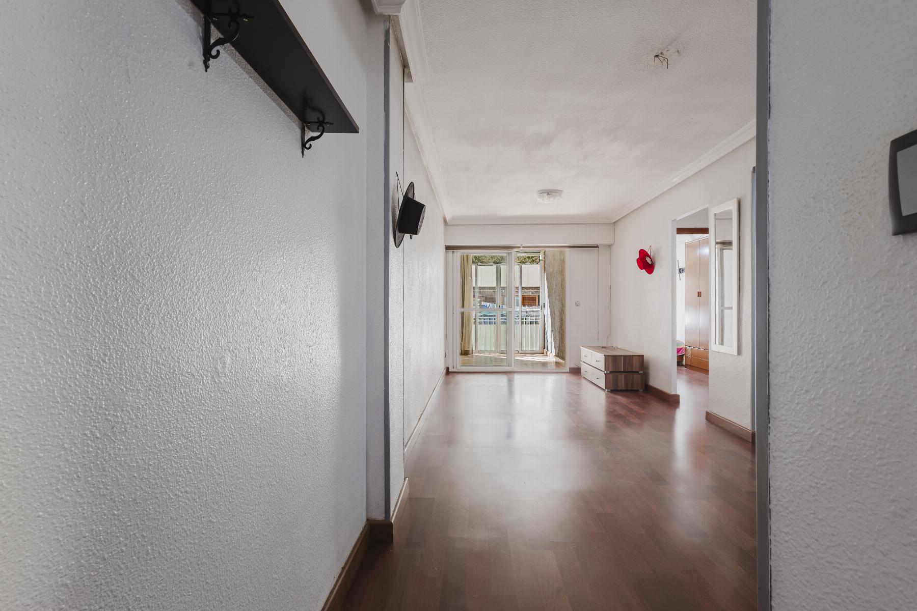 Bright hallway with wood floor leading to glass doors opening to a balcony; red wall decor and a small dresser on the right side.