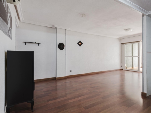 Spacious, minimally furnished living room with white walls, a black cabinet, wall shelf, and a sliding glass door to a balcony on the right.