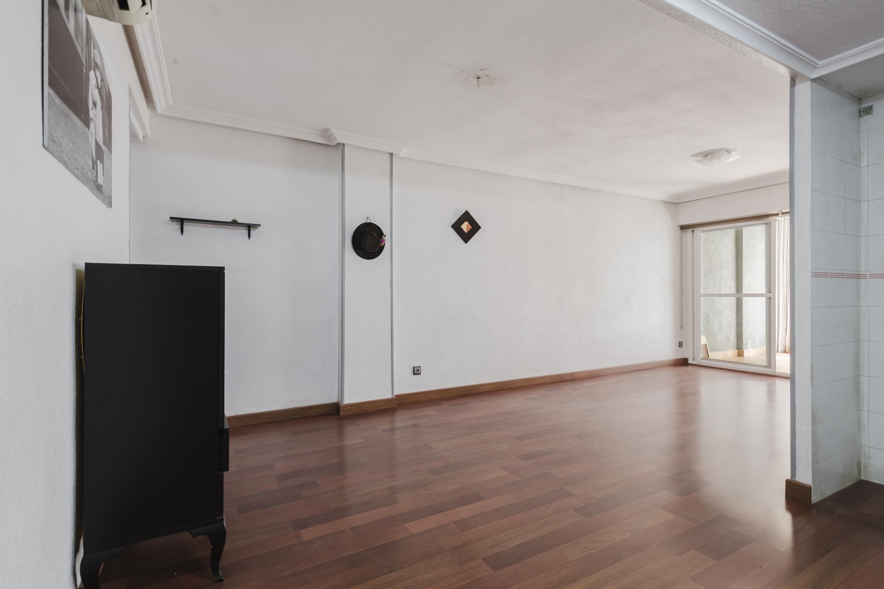 Spacious, minimally furnished living room with white walls, a black cabinet, wall shelf, and a sliding glass door to a balcony on the right.