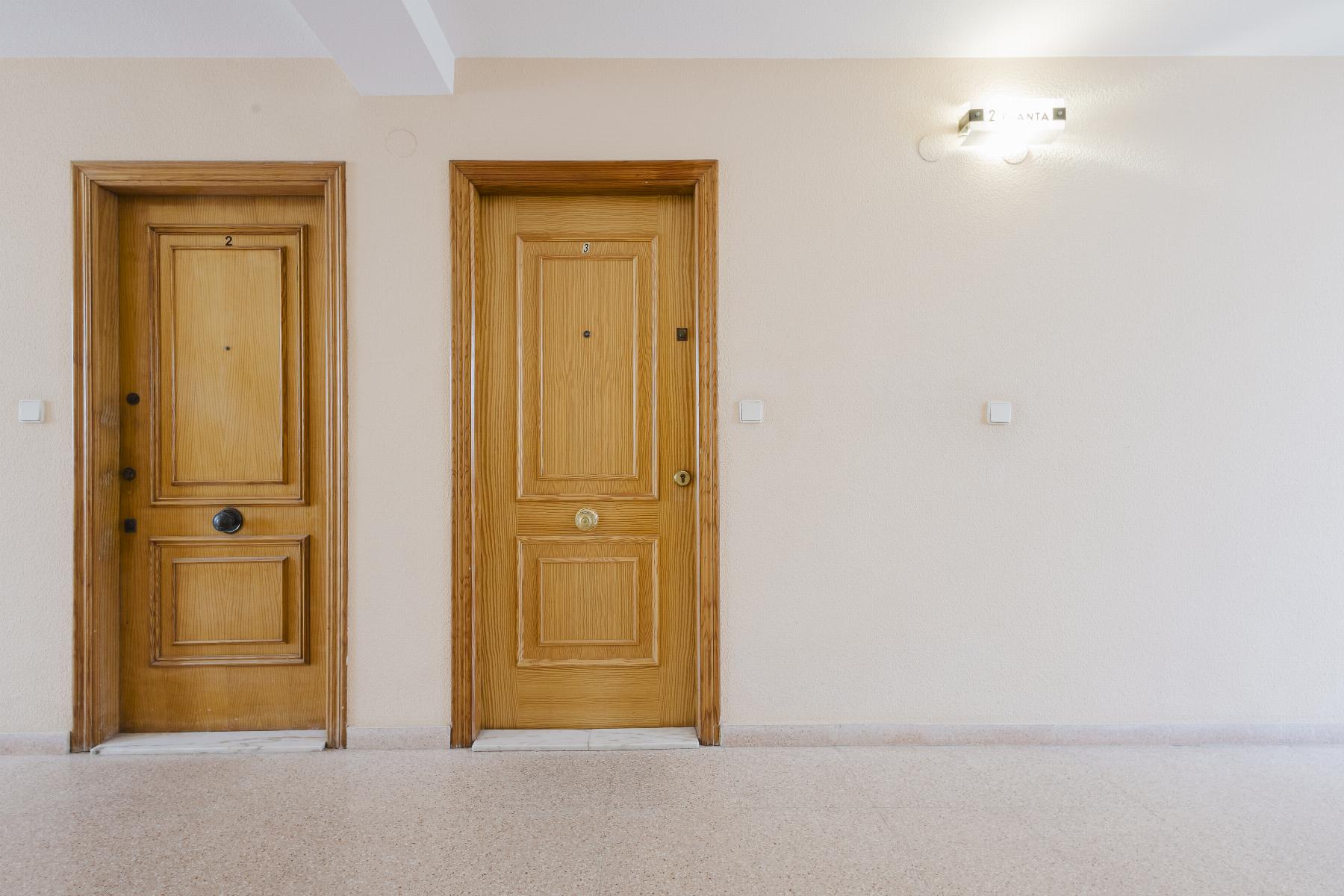 Two wooden apartment doors labeled 2 and 3 in a beige hallway with a wall light on the right side