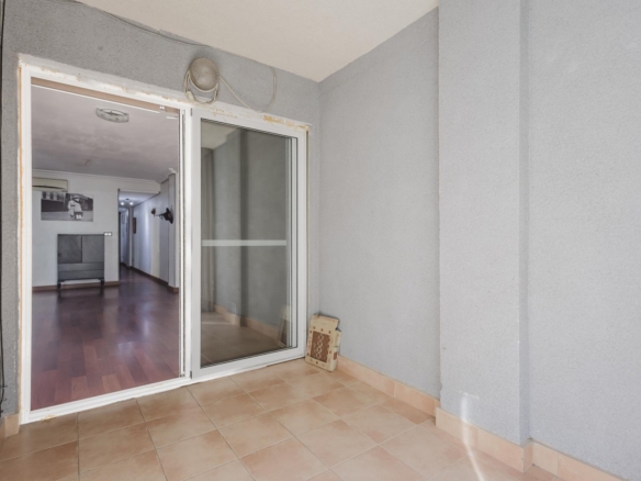 Balcony with beige tiled floor and gray walls, sliding glass door to a living room visible inside.