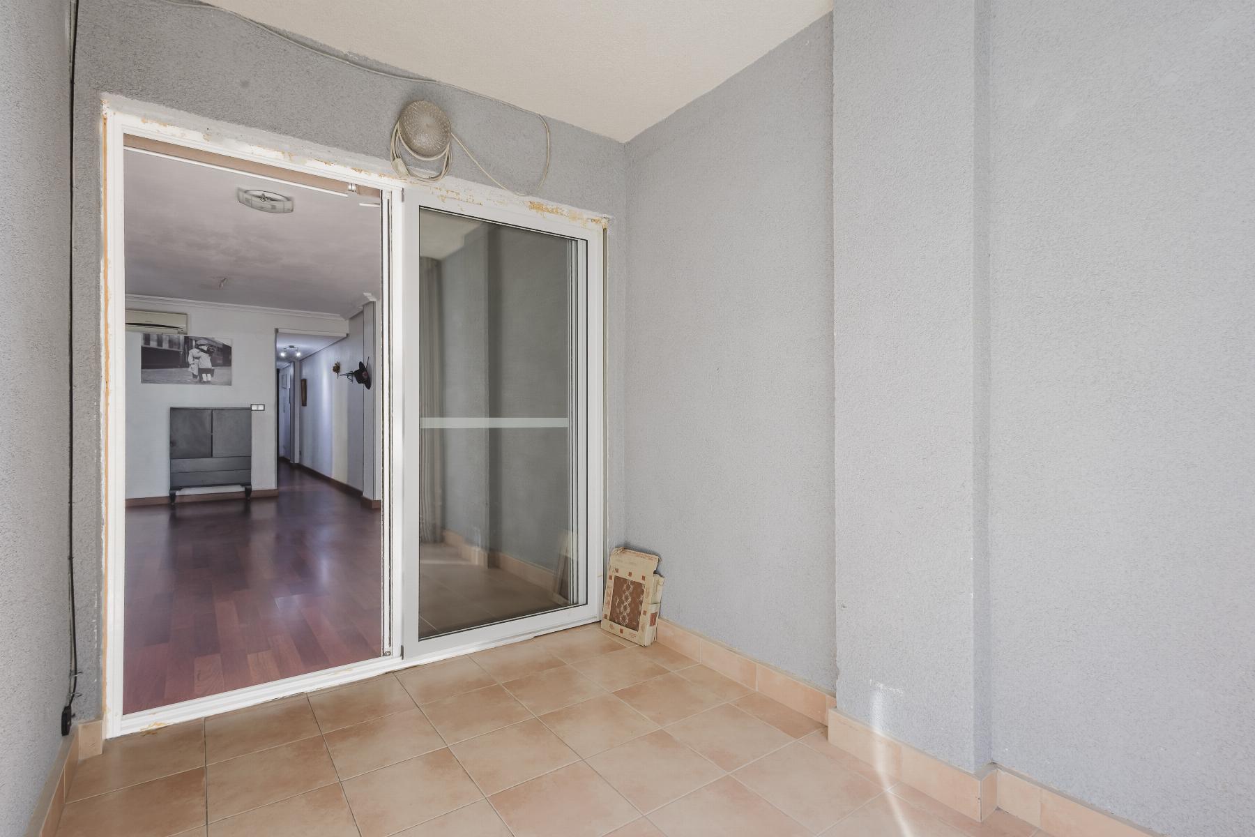 Balcony with beige tiled floor and gray walls, sliding glass door to a living room visible inside.