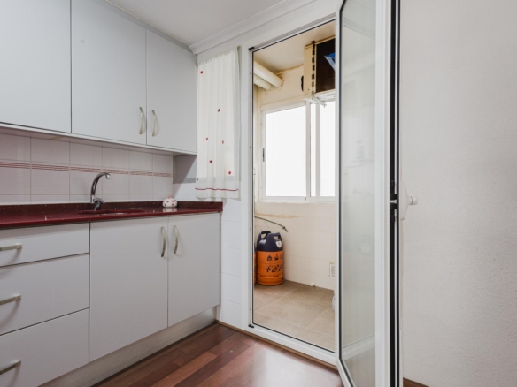 Kitchen with white cabinets, red countertop, and a sink along tiled backsplash, leading to a balcony through glass doors.