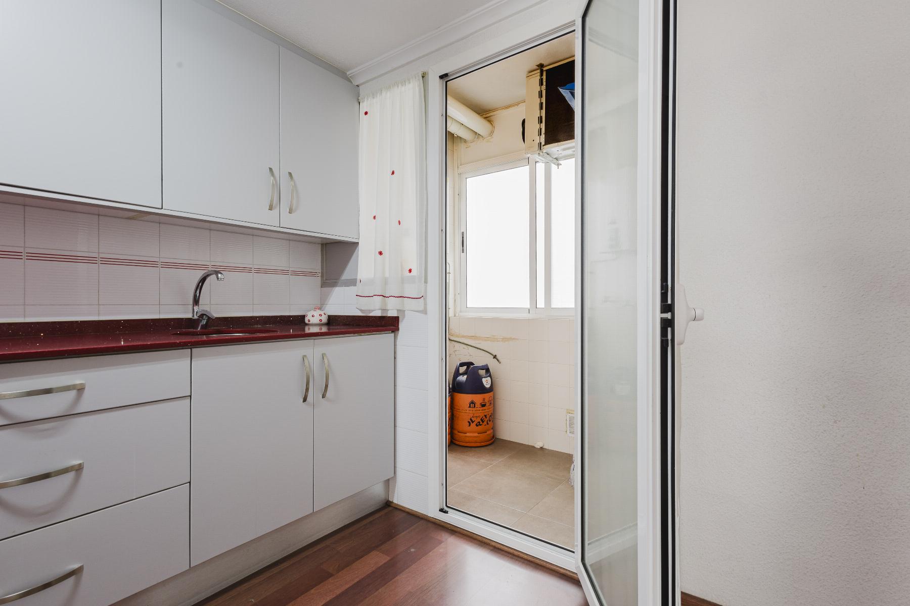 Kitchen with white cabinets, red countertop, and a sink along tiled backsplash, leading to a balcony through glass doors.