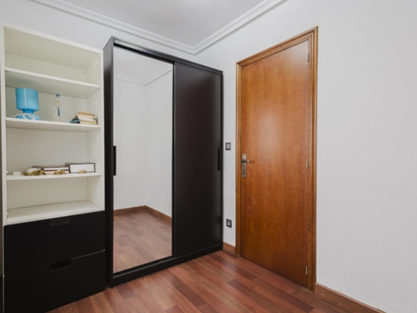 Black sliding-door wardrobe with a large mirror sits in a hallway beside a wooden door; its open white shelves hold a few items.