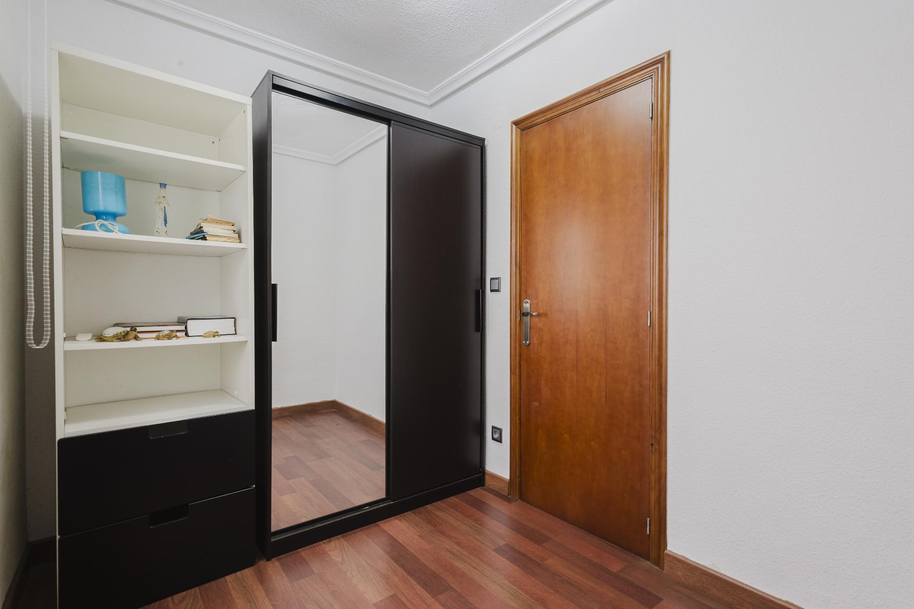 Black sliding-door wardrobe with a large mirror sits in a hallway beside a wooden door; its open white shelves hold a few items.