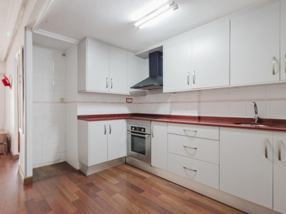 Bright kitchen with white cabinets, red speckled countertop, and stainless steel oven beneath a range hood.
