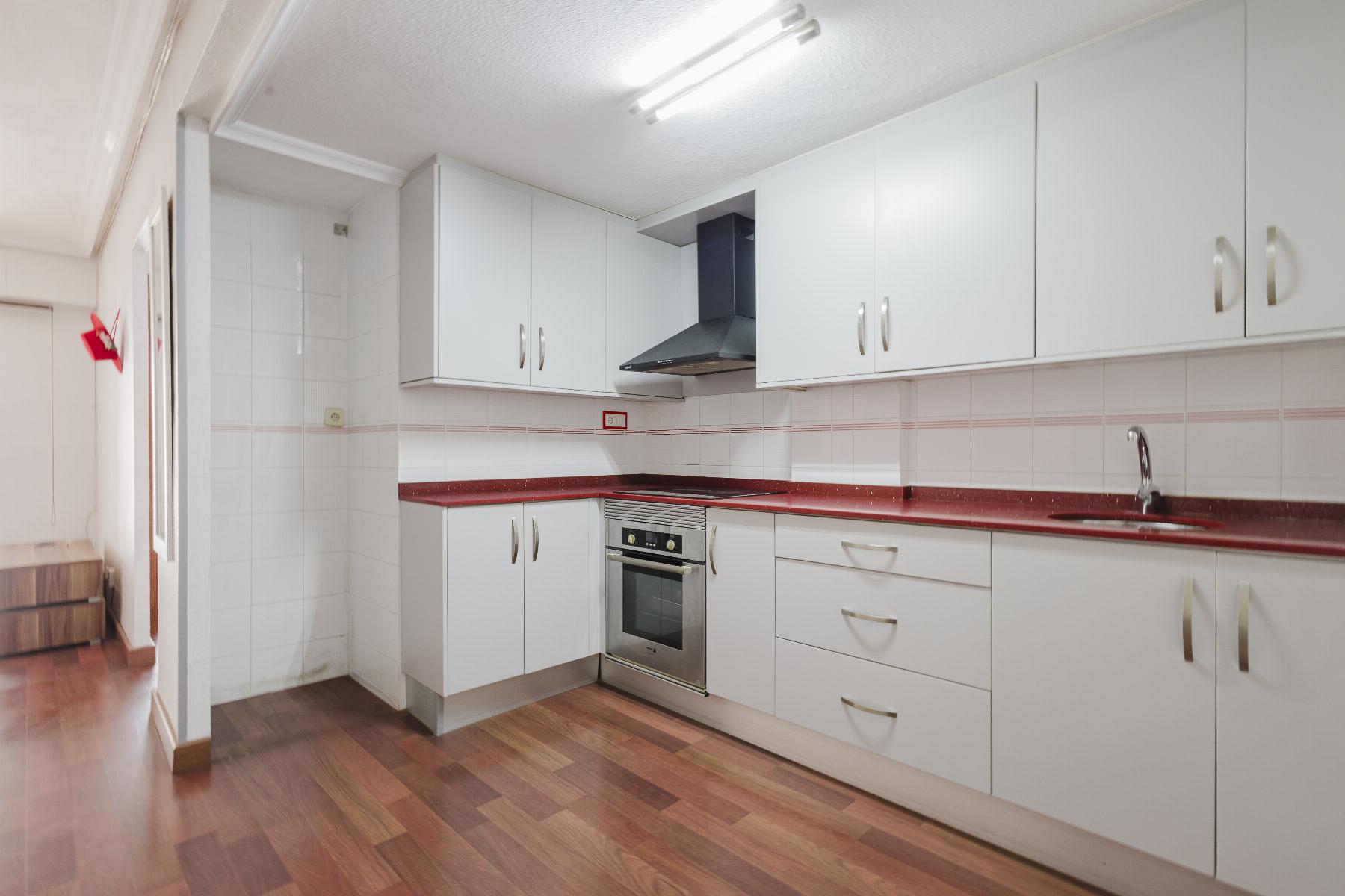 Bright kitchen with white cabinets, red speckled countertop, and stainless steel oven beneath a range hood.