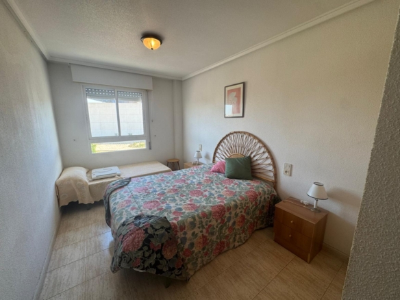 Cozy bedroom with a bed covered in a floral quilt, wicker headboard, two nightstands with lamps, and a window letting in light.
