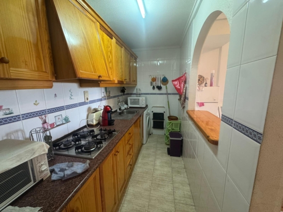 Narrow galley kitchen with wooden cabinets on the left, a gas stove, sink, microwave, and laundry area at the far end.