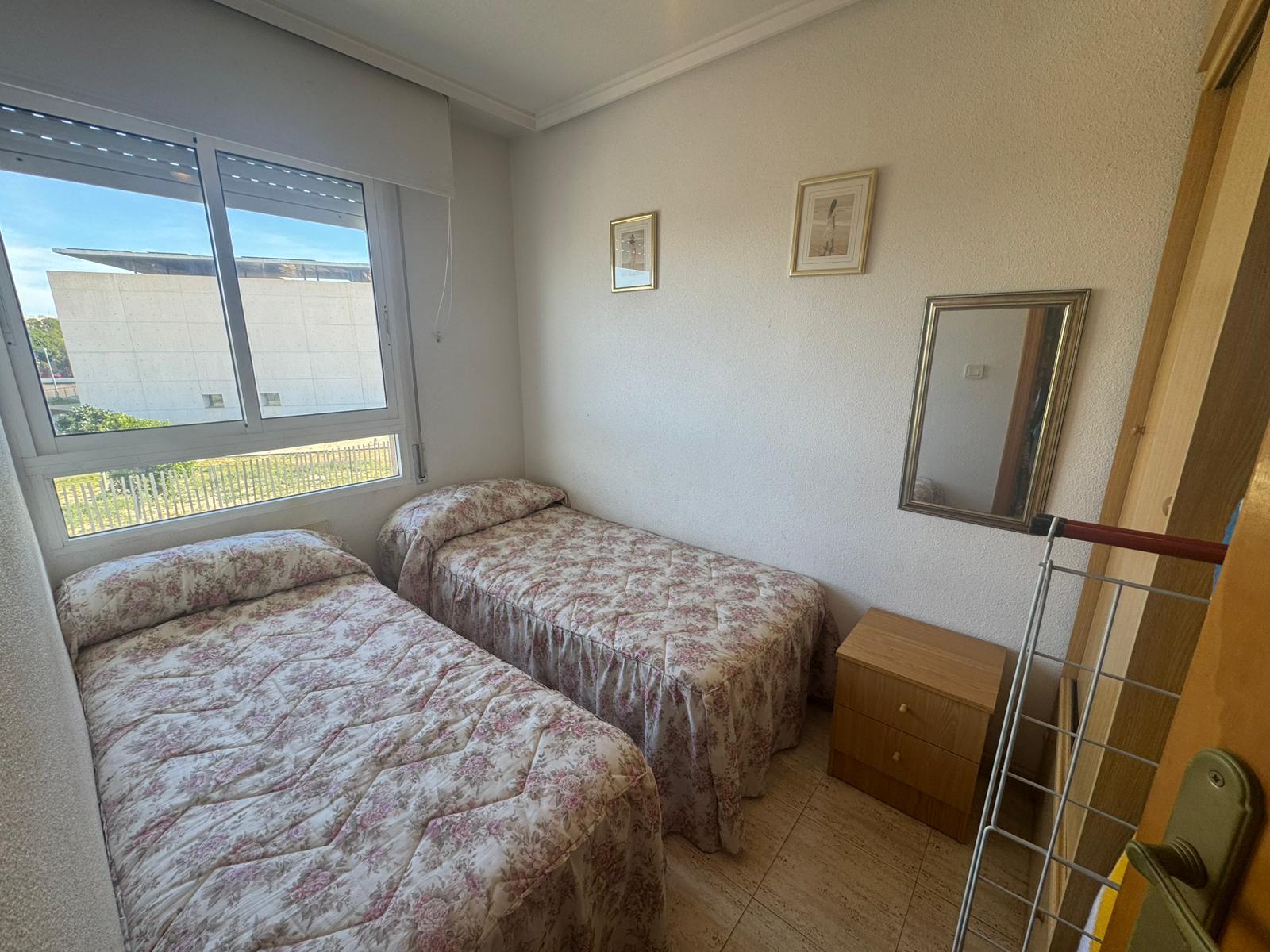 Small bedroom with two single beds covered in pink floral quilts near a large window.