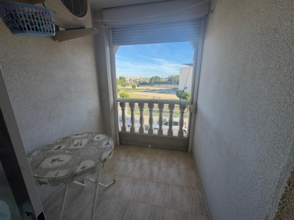 Narrow balcony with a round patterned table, a metal chair, and a cityscape beyond the white balustrade.