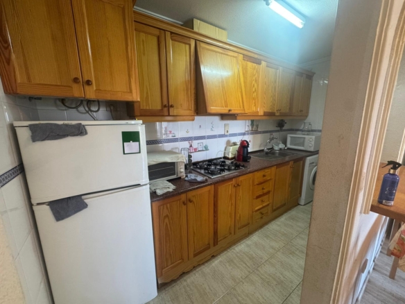 Long row of wooden kitchen cabinets above a brown countertop with a gas stove and small appliances in a compact kitchen.