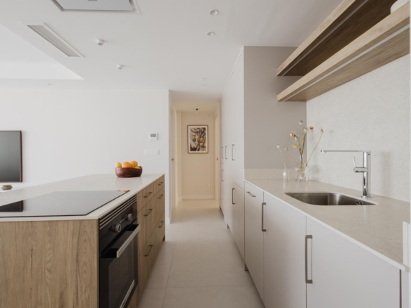 Bright, modern kitchen with a white and wood island, white cabinets, and a hallway at the far end.