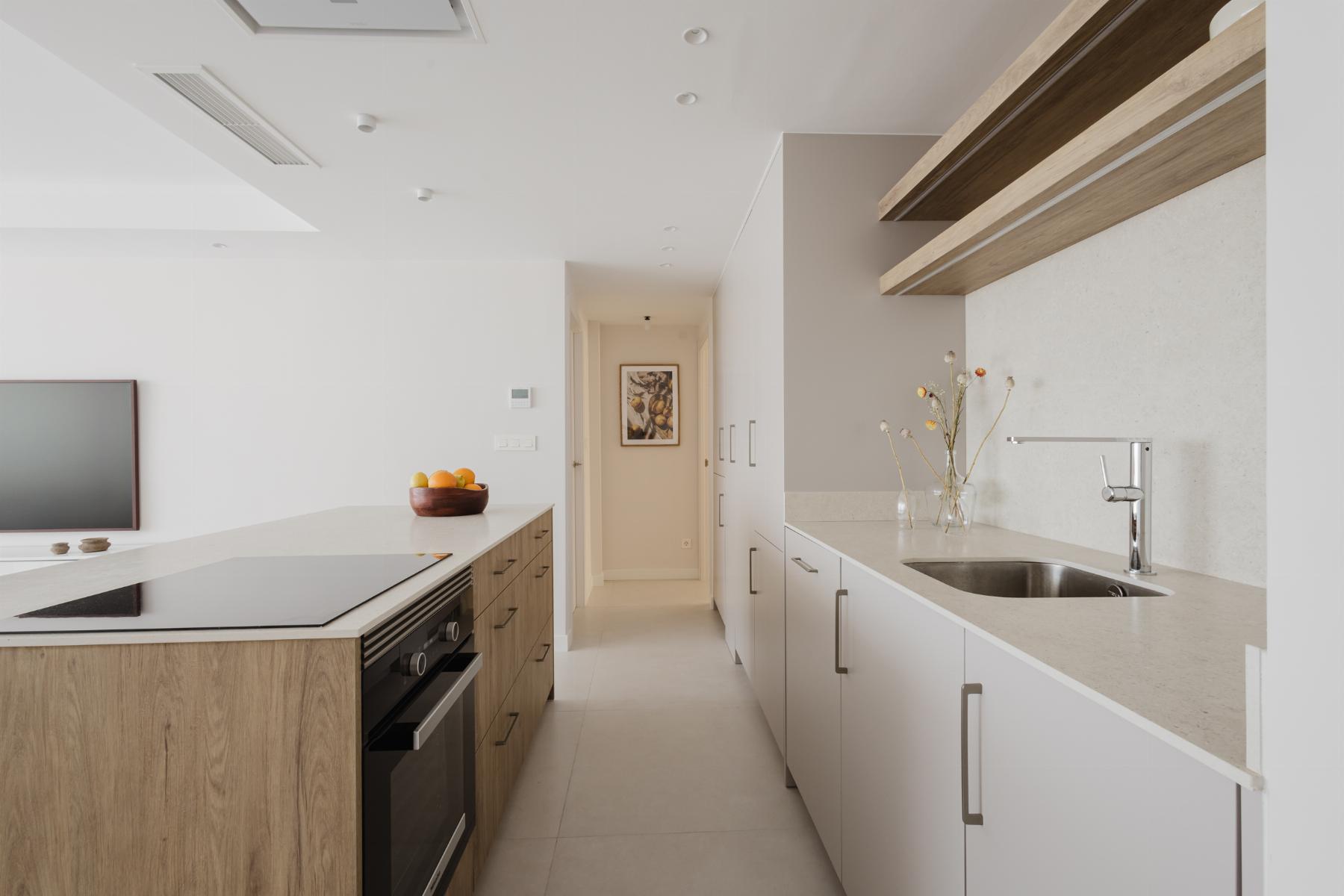 Bright, modern kitchen with a white and wood island, white cabinets, and a hallway at the far end.
