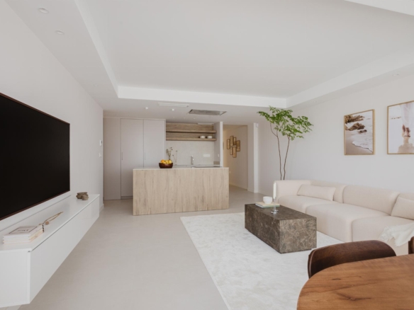 Open-plan living area with a large wall-mounted TV, white console, beige sectional sofa, and a wooden coffee table.