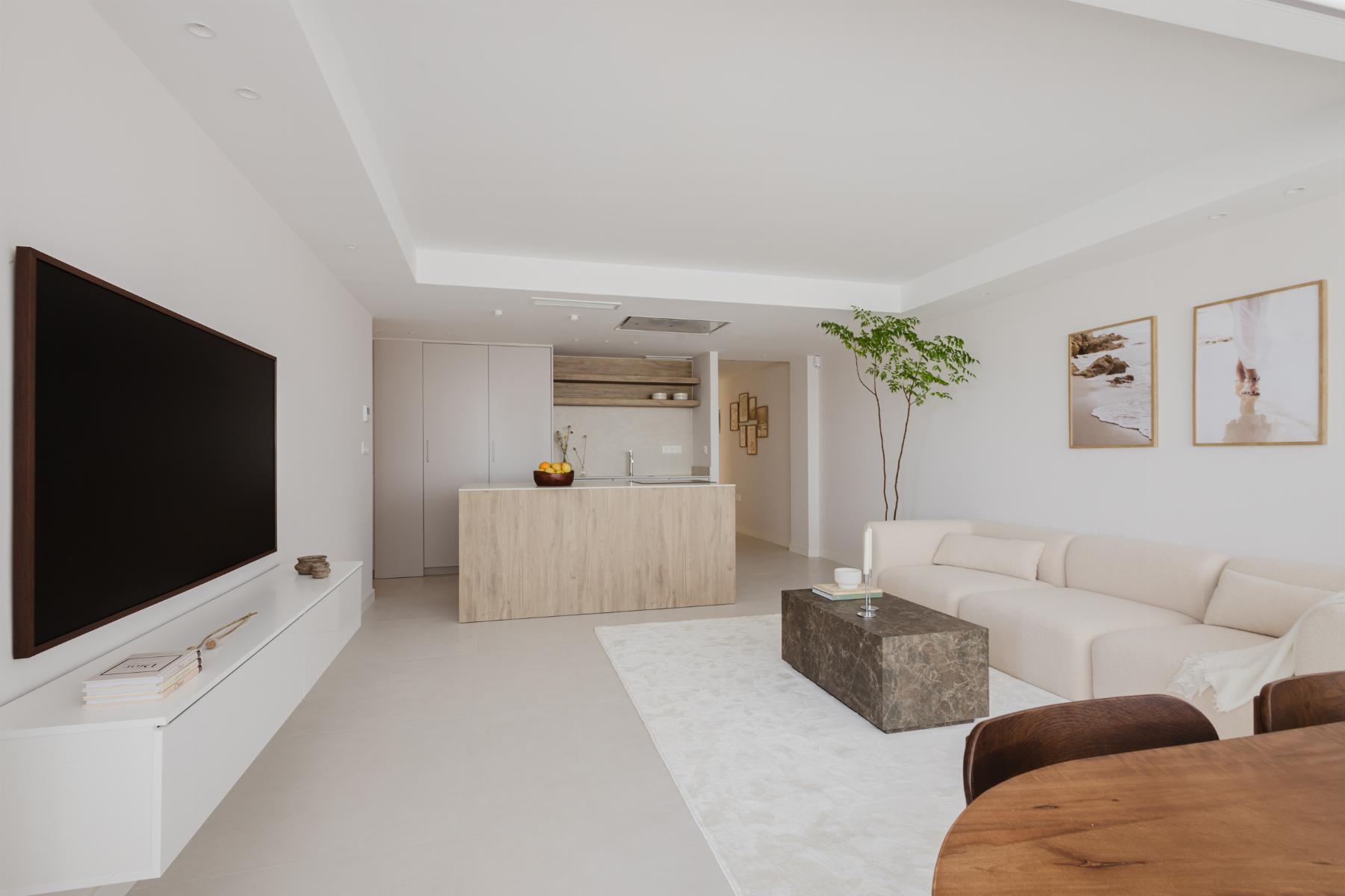 Open-plan living area with a large wall-mounted TV, white console, beige sectional sofa, and a wooden coffee table.