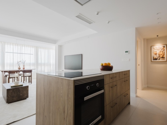 Open-plan kitchen with a wood-tone island, built-in oven, and a bowl of fruit on the counter.