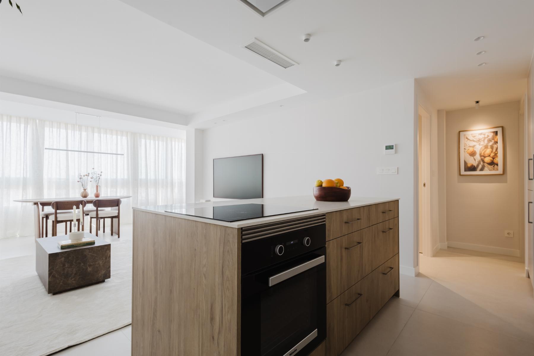 Open-plan kitchen with a wood-tone island, built-in oven, and a bowl of fruit on the counter.