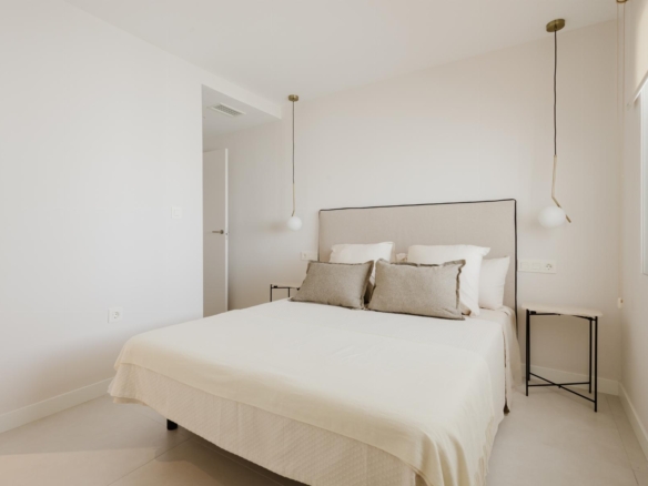 Minimalist white bedroom with a beige upholstered headboard bed, white bedding, and two hanging pendant lights by each side.
