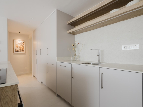 Modern white kitchen with light wood open shelves and a stainless sink area, hallway beyond with framed art