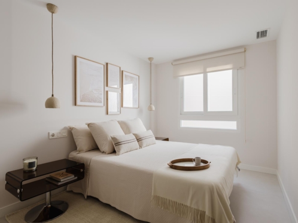Bright minimalist bedroom with a white bed, beige pillows, and two hanging pendant lamps by the headboard wall art.