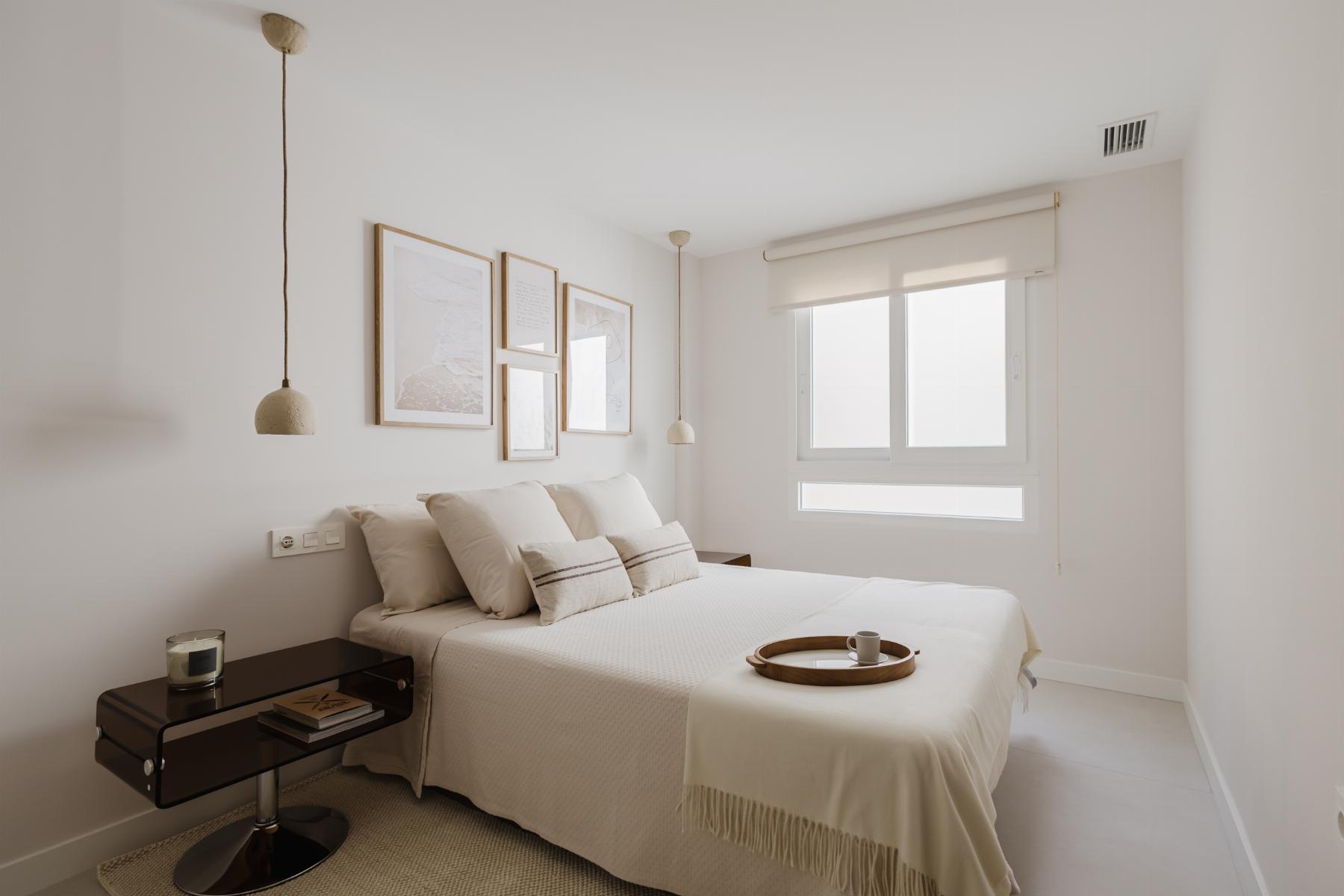 Bright minimalist bedroom with a white bed, beige pillows, and two hanging pendant lamps by the headboard wall art.