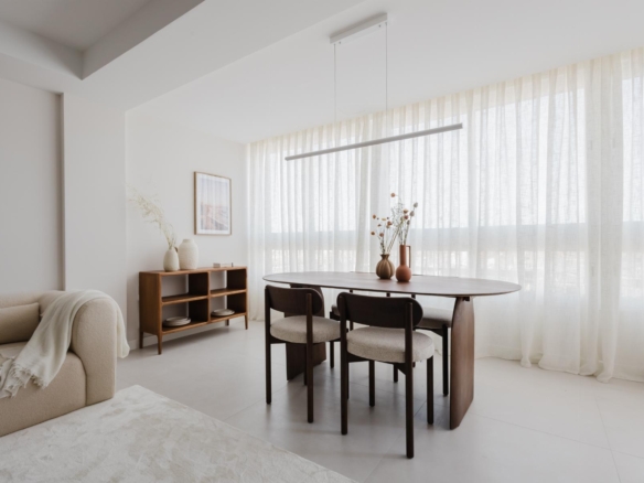Bright minimalist dining area with a round wooden table, four dark chairs, and sheer white curtains