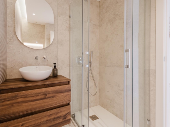 Modern bathroom with a round white vessel sink on a wooden vanity and a glass-enclosed shower.