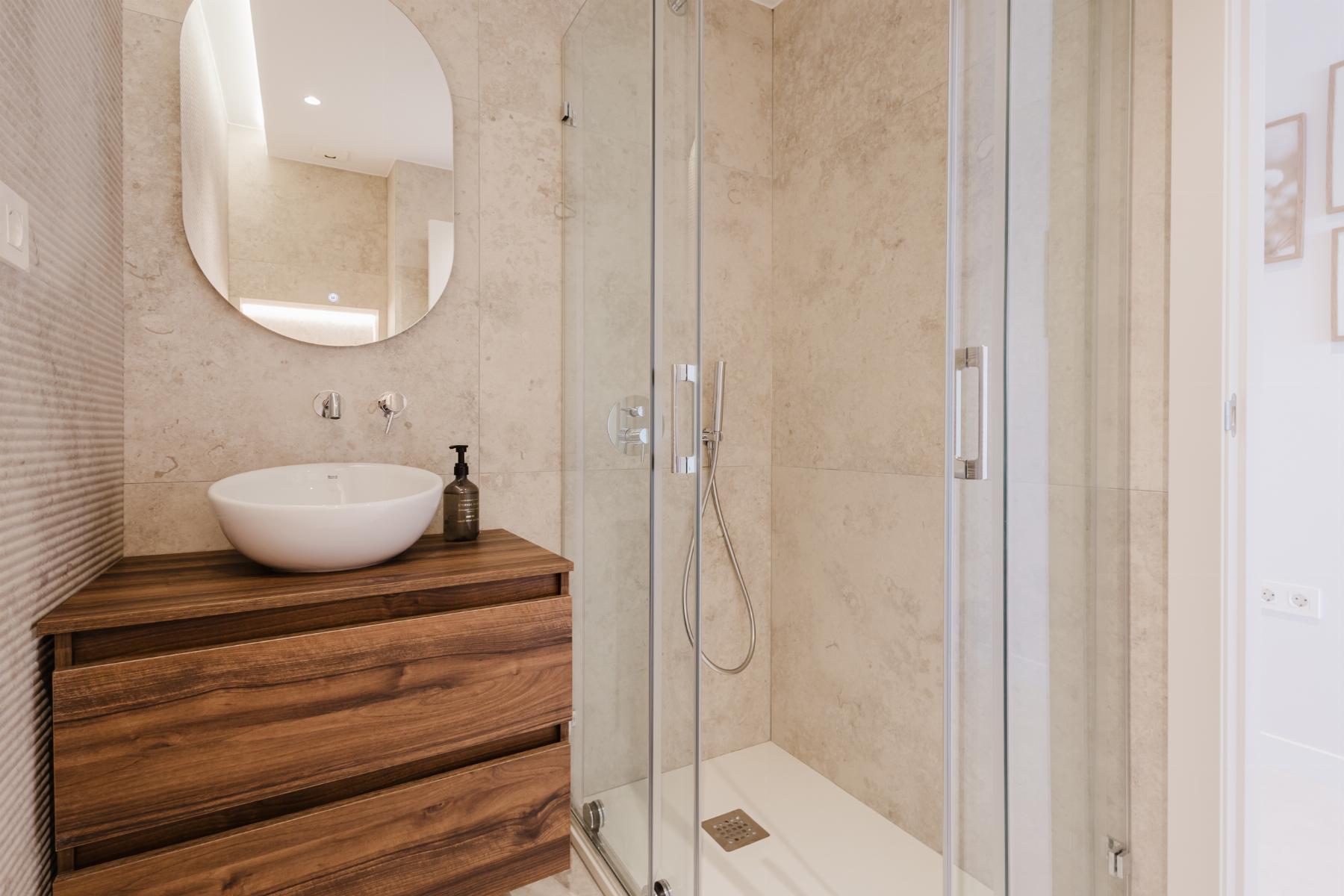 Modern bathroom with a round white vessel sink on a wooden vanity and a glass-enclosed shower.