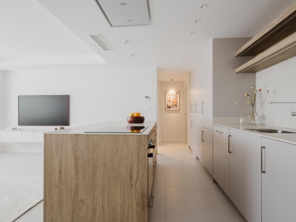 Bright white modern kitchen with a wooden island, gray lower cabinets, built-in appliances, and a bowl of fruit on the island.