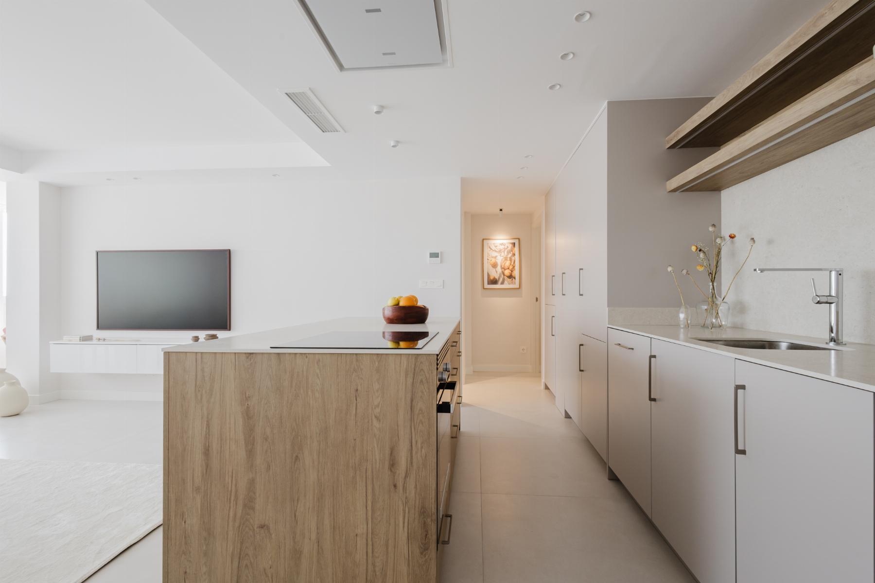 Bright white modern kitchen with a wooden island, gray lower cabinets, built-in appliances, and a bowl of fruit on the island.