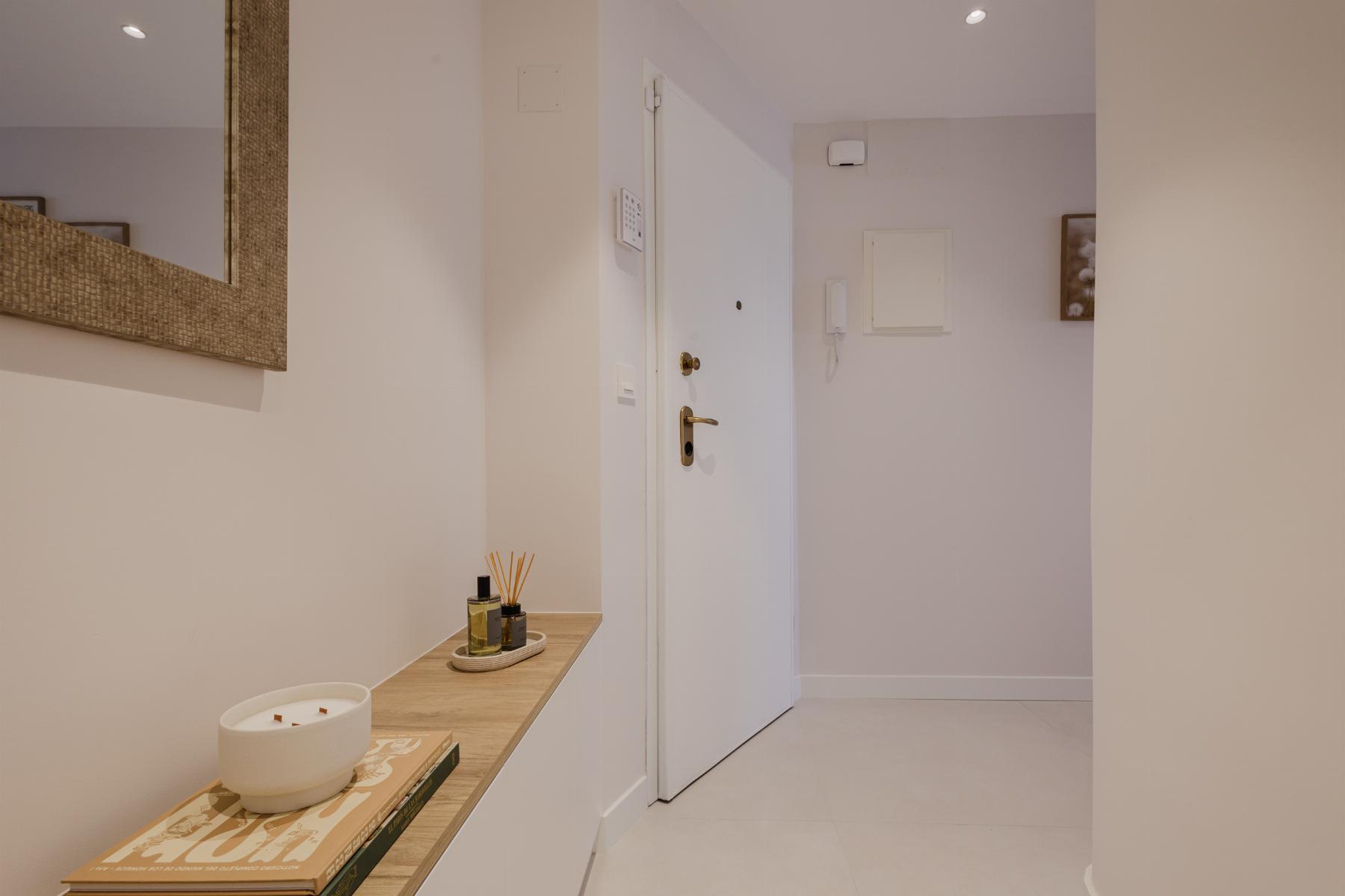Modern hallway with white walls, a wooden console table, candle and reed diffuser, and a white front door in the center.