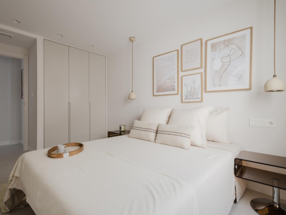 Minimalist white bedroom with a large bed, neutral bedding, and four framed pictures above the headboard.