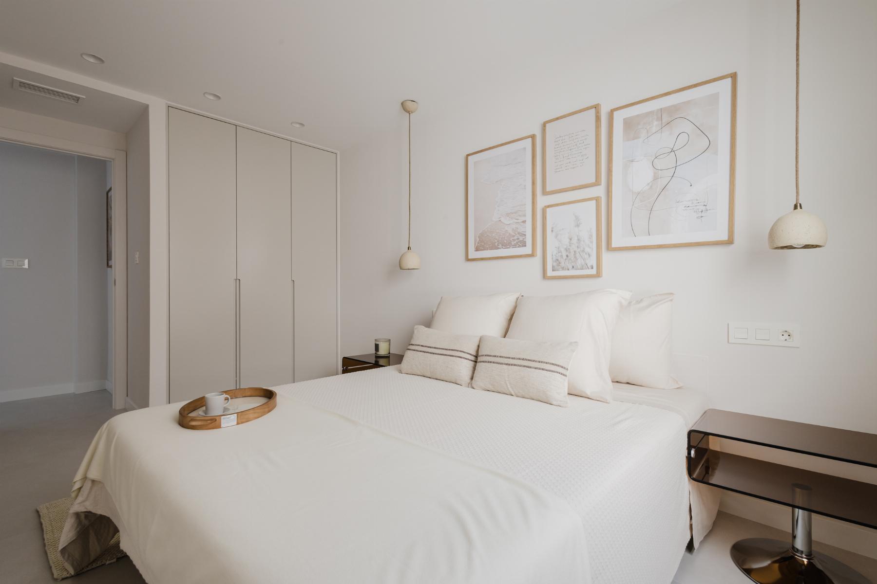 Minimalist white bedroom with a large bed, neutral bedding, and four framed pictures above the headboard.