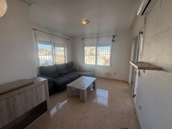 Living room with a gray sectional sofa, light wood coffee table, and a cabinet, near large windows with bars and an outdoor view.
