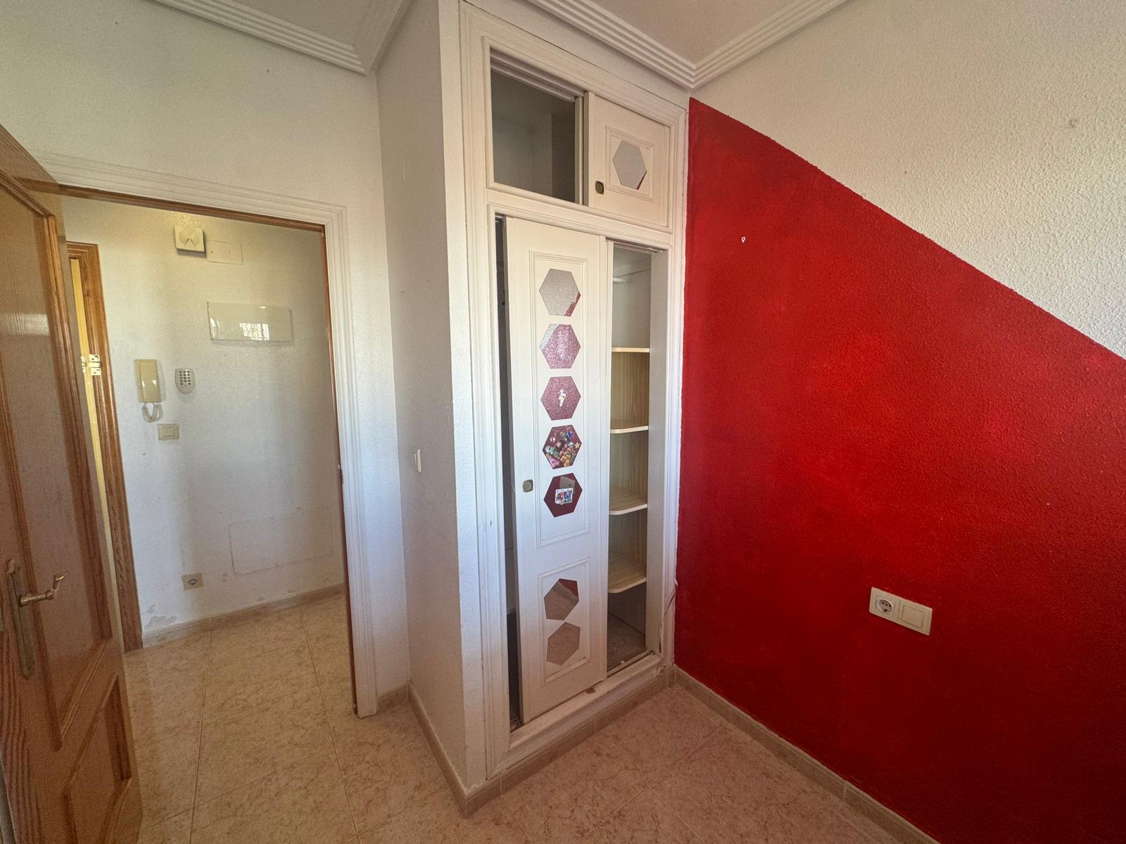 Hallway with a red diagonal wall, a white built-in cabinet with hexagon stickers, and open shelving nearby.