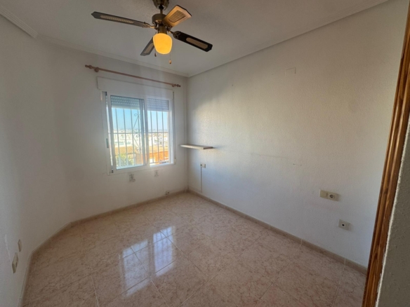 Small empty room with tiled floor, white walls, a window with bars, and a ceiling fan with a light fixture above.